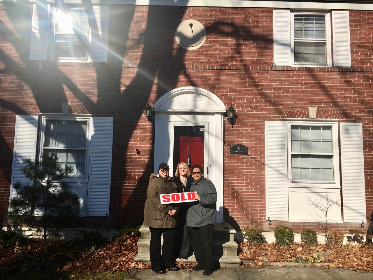 Happy Couple Holding a "SOLD" Sign Celebrate in front of their new home