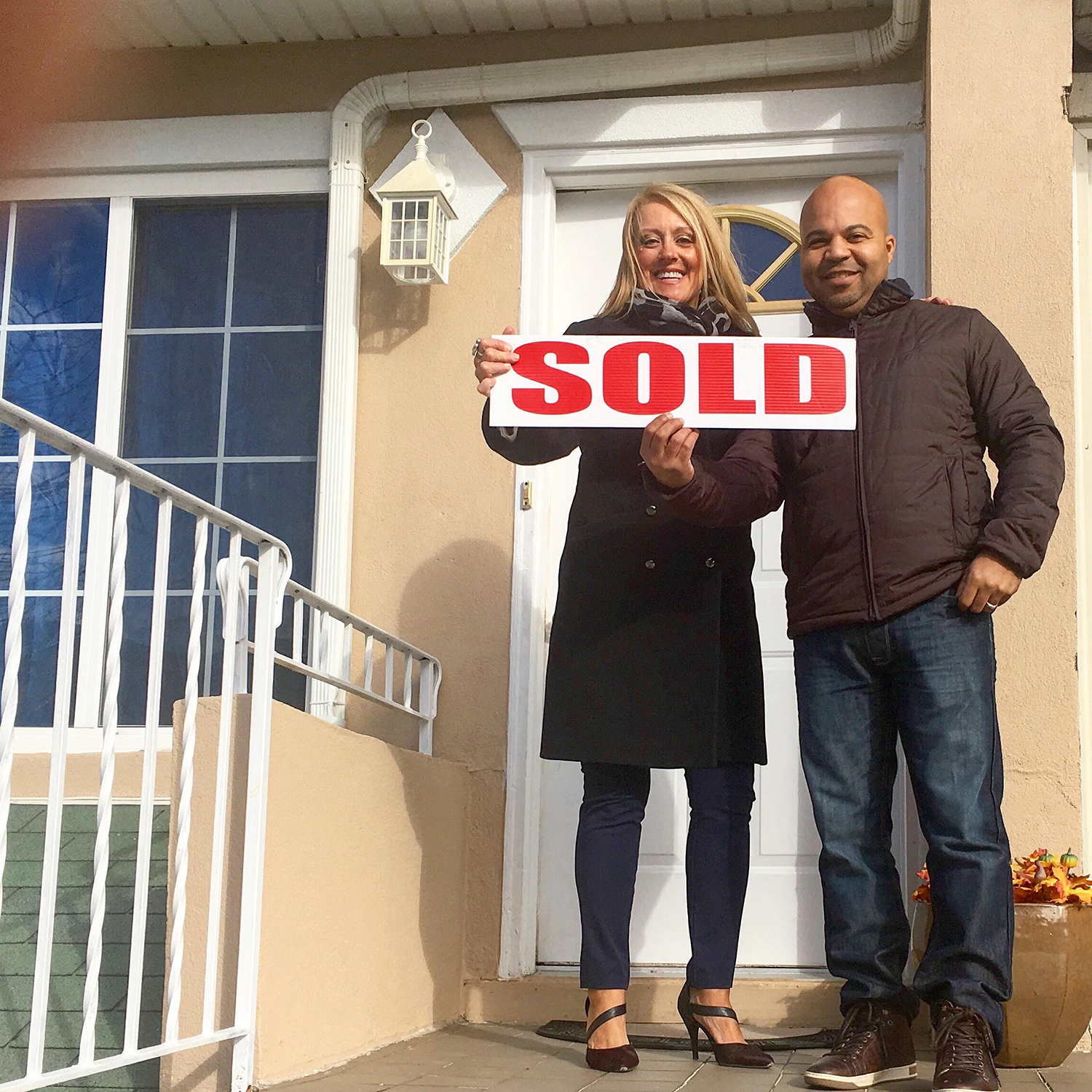 Holly poses with a happy client while holding an over-sized "Sold" sign