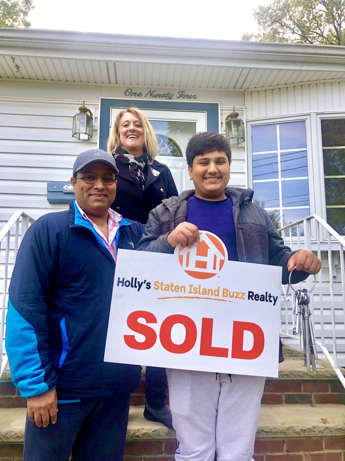 Happy buyer standing with Holly and family in front of a sold Westerleigh home with a Holly’s Staten Island Buzz Realty SOLD sign.