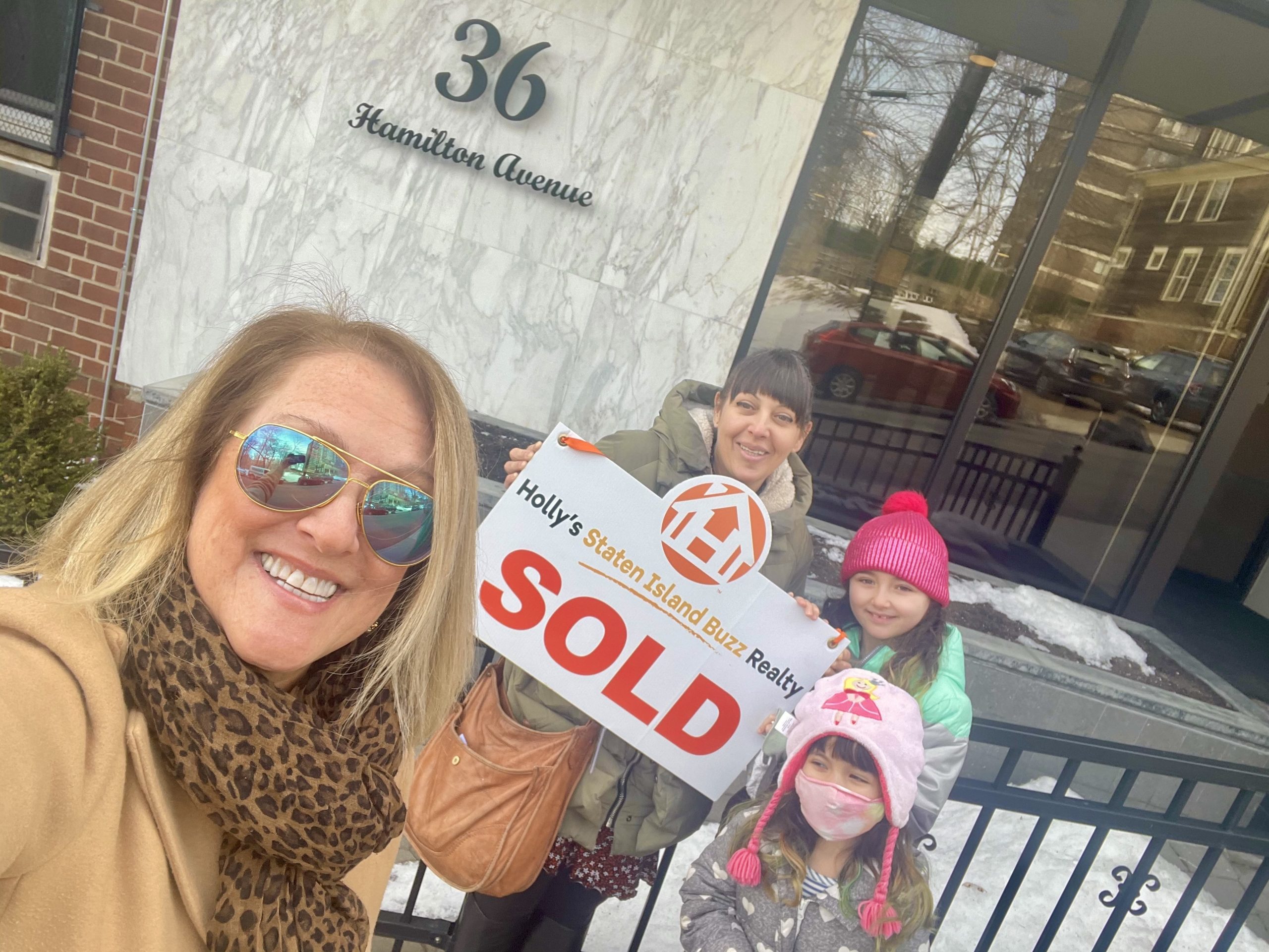Holly with happy client Lauren and her family holding a sold sign outside 36 Hamilton Avenue in St. George, Staten Island.